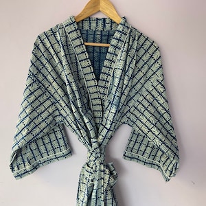 Könnte beinhalten: Eine blaue und weiße gemusterte Robe mit einem Bindeverschluss. Die Robe hat ein geometrisches Muster mit weißem Hintergrund und blauen Linien.