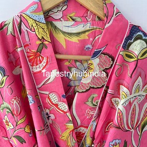 May include: Pink cotton robe with a floral print and white piping. The robe has a shawl collar and a tie closure. The fabric is soft and comfortable.