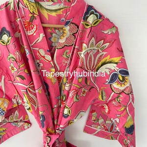 May include: A pink cotton robe with a floral print and a white trim. The robe has a tie belt and two pockets. The text "Tapestryhubindia" is visible on the robe.