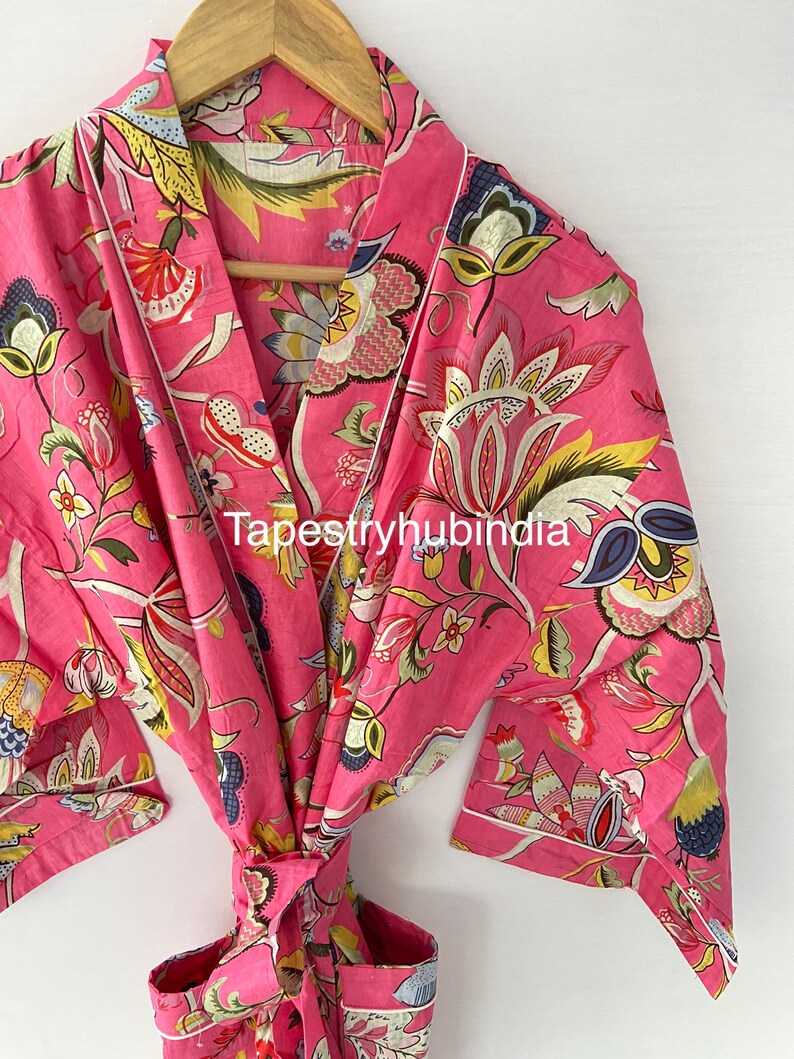 May include: A pink cotton robe with a floral print and a white trim. The robe has a tie belt and two pockets. The text "Tapestryhubindia" is visible on the robe.