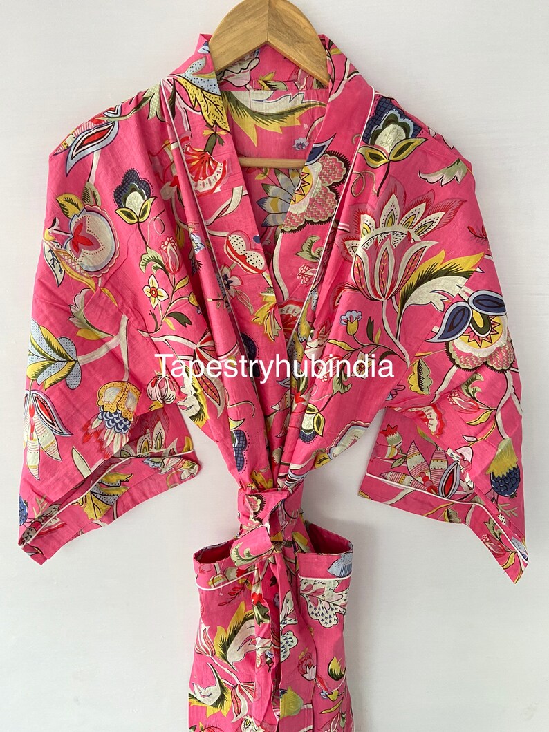 May include: Pink floral cotton robe with a white trim and a tie belt. The robe has a floral pattern with yellow, green, and blue accents. The text "Tapestryhubindia" is visible on the robe.