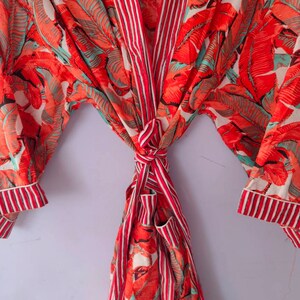 Op de afbeelding: Een rood-wit gestreepte badjas met een tropische bladerenprint. De badjas is in de taille gebonden en heeft lange mouwen.