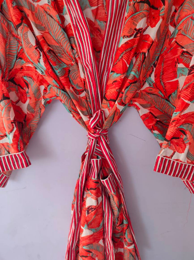 Op de afbeelding: Een rood-wit gestreepte badjas met een tropische bladerenprint. De badjas is in de taille gebonden en heeft lange mouwen.