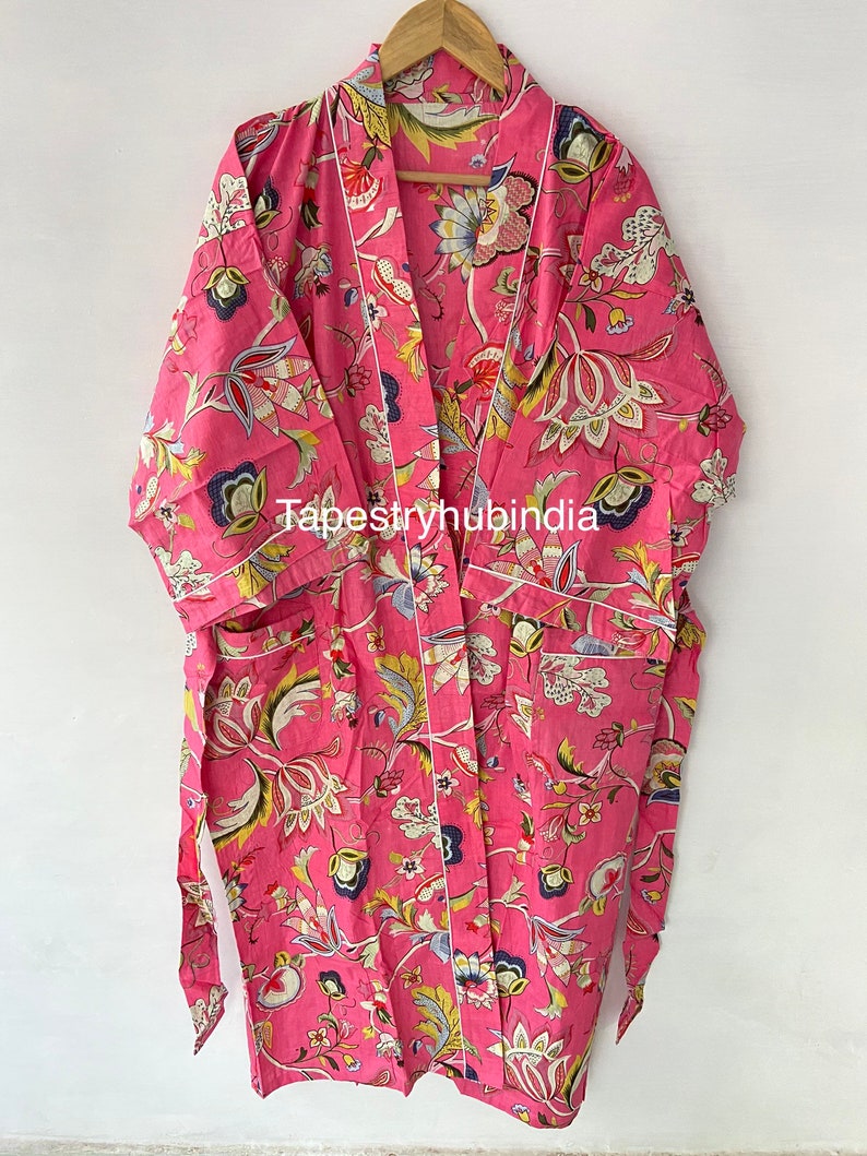 May include: A pink floral print robe with a white trim and a matching tie belt. The robe has a pocket on the left side and the text "Tapestryhubindia" is printed on the front.