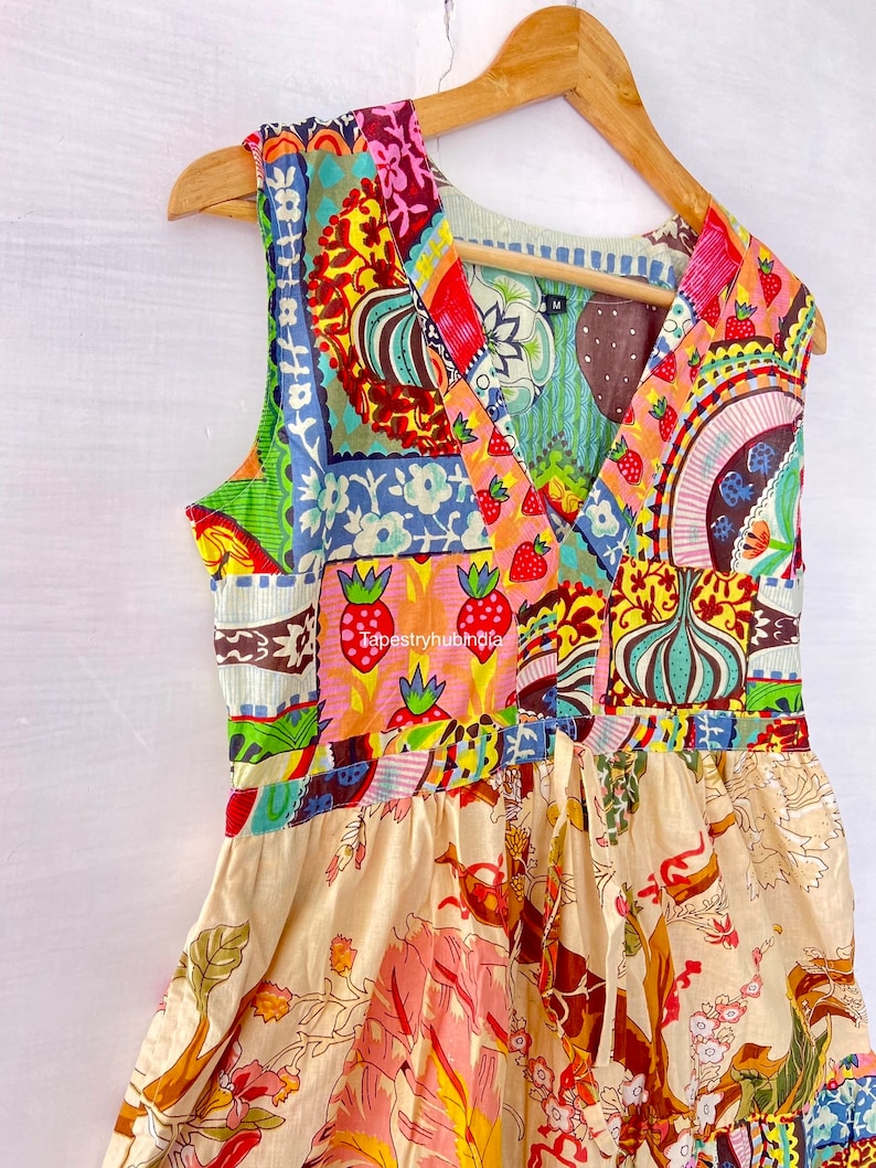 Op de afbeelding: Een mouwloze jurk met een patchwork-ontwerp met een verscheidenheid aan kleurrijke patronen en bloemenmotieven. De jurk heeft een V-hals en een geplooide rok. De stof is een mix van katoen en linnen.