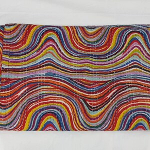 May include: A folded textile with a vibrant, wavy pattern. The design incorporates horizontal stripes in red, orange, yellow, green, blue, and purple. The edges are finished with a red border and white stitching.