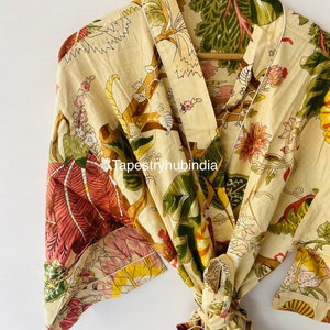 Puede incluir: Una bata de color crema con estampado floral con flores verdes, rosas y amarillas. La bata tiene cierre de lazo y un ribete blanco.