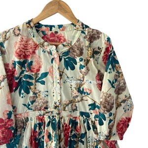 May include: A white cotton dress with a floral print featuring pink, red, and teal flowers. The dress has a button-up front and a ruffled hem.