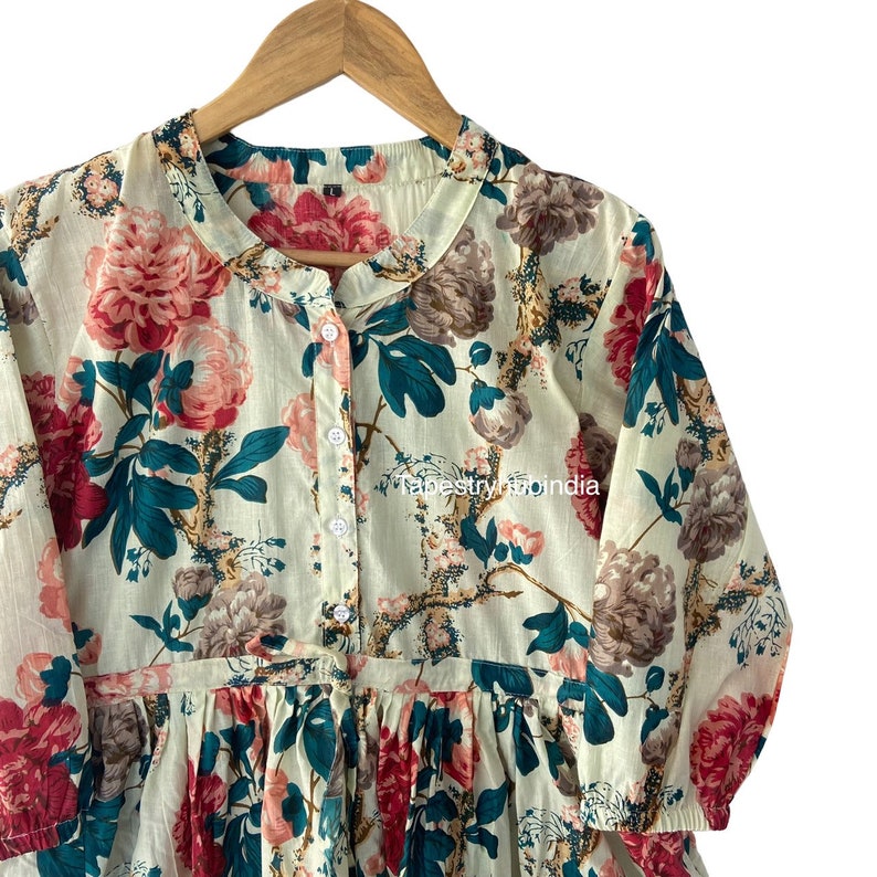May include: A white cotton dress with a floral print featuring pink, red, and teal flowers. The dress has a button-up front and a ruffled hem.