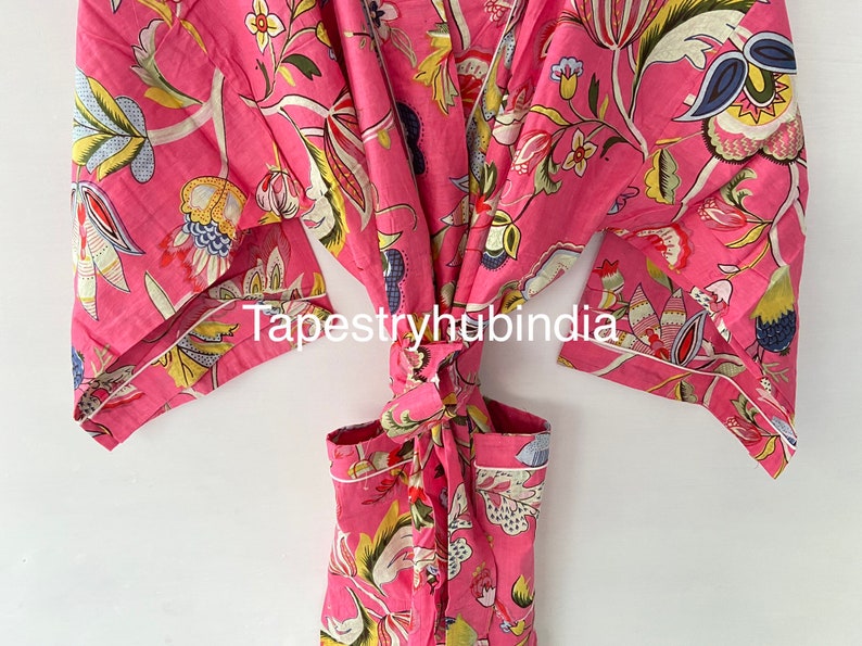 May include: Pink cotton robe with a floral print and a tie belt. The robe has a pocket on the front. The text "Tapestryhubindia" is printed on the robe.