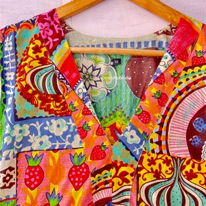 Op de afbeelding: Een kleurrijke patchwork jurk met een V-hals en een strik in de taille. De jurk heeft verschillende patronen, waaronder bloemen, geometrische en abstracte ontwerpen. De jurk is gemaakt van katoen en is verkrijgbaar in maat M. De tekst "Tapestryhubindia" is zichtbaar op de jurk.