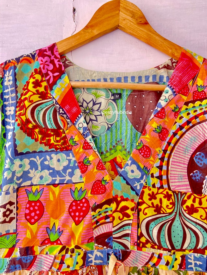 Op de afbeelding: Een kleurrijke patchwork jurk met een V-hals en een strik in de taille. De jurk heeft verschillende patronen, waaronder bloemen, geometrische en abstracte ontwerpen. De jurk is gemaakt van katoen en is verkrijgbaar in maat M. De tekst "Tapestryhubindia" is zichtbaar op de jurk.