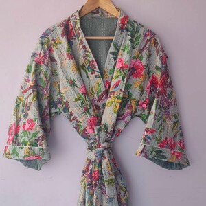 May include: A floral patterned robe with a long tie belt. The robe is made of a soft, lightweight fabric and has a relaxed fit. The fabric is a light blue colour with a subtle texture. The floral pattern is in shades of pink, red, purple, and green.