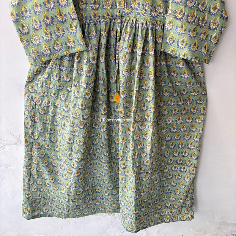 May include: A green cotton dress with a yellow and blue floral print. The dress has a gathered waist and a tie at the neckline.