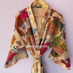 Puede incluir: Una bata de algodón beige con estampado floral y cinturón de lazo. La bata tiene un ribete blanco y está acolchada.