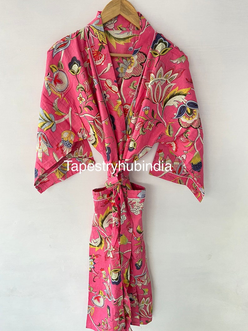 May include: A pink floral print cotton robe with a tie belt and long sleeves. The robe has a floral pattern with yellow, blue, and green accents. The text "Tapestryhubindia" is visible on the robe.