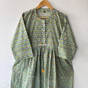 May include: A green cotton dress with a floral print and a tie at the waist. The dress has a button-up front and three-quarter sleeves.
