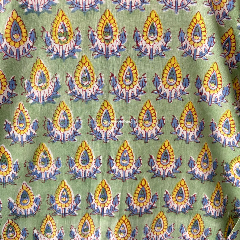 May include: Green fabric with a repeating pattern of yellow, blue, and red floral motifs. The fabric has a subtle texture.