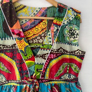 May include: A colourful sleeveless dress with a V-neckline and a tie at the waist. The dress is made of a patchwork of different fabrics with floral and geometric patterns in shades of red, blue, green, yellow, and brown. The dress has a white trim around the neckline and armholes. The text "TapestryHubIndia" is visible on the dress.