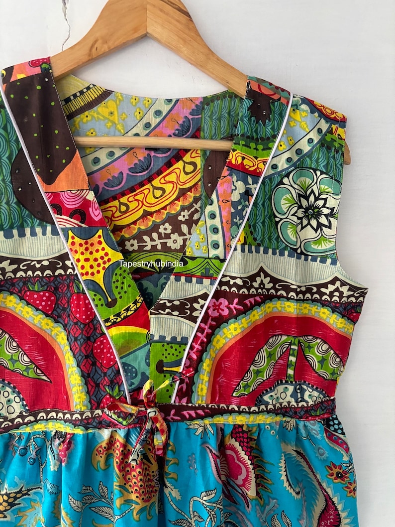 May include: A colourful sleeveless dress with a V-neckline and a tie at the waist. The dress is made of a patchwork of different fabrics with floral and geometric patterns in shades of red, blue, green, yellow, and brown. The dress has a white trim around the neckline and armholes. The text "TapestryHubIndia" is visible on the dress.
