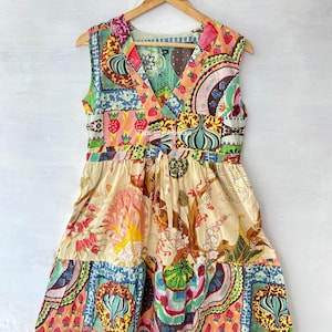 Może przedstawiać: Kolorowa sukienka w stylu patchwork z dekoltem w kształcie litery V i rozkloszowaną spódnicą. Sukienka jest wykonana z bawełny i ma kwiatowy wzór. Sukienka jest bez rękawów i ma wiązanie w talii.