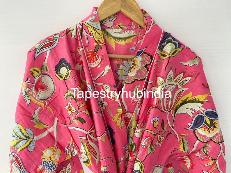 May include: A pink cotton robe with a floral print. The robe has a white trim and a tie belt. The text "Tapestryhubindia" is printed on the robe.