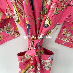 May include: A pink cotton robe with a floral print and white piping. The robe is tied at the waist and has a pocket on the left side. The text "Tapestryhubindia" is visible on the robe.