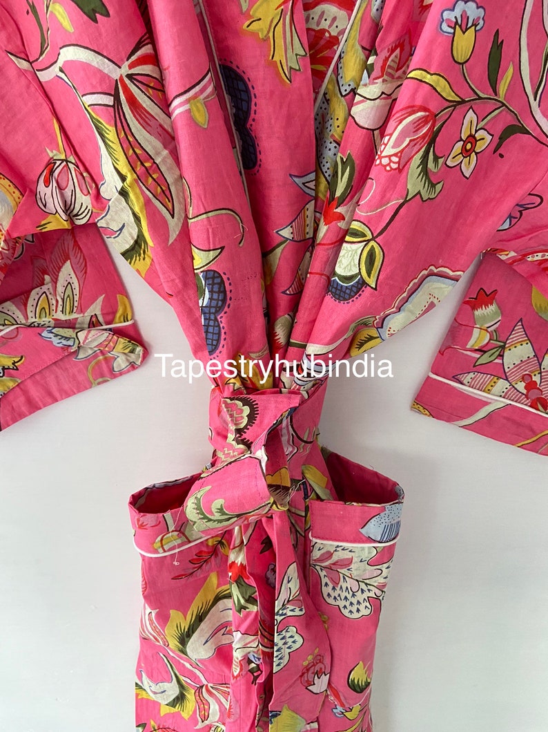 May include: A pink cotton robe with a floral print and white piping. The robe is tied at the waist and has a pocket on the left side. The text "Tapestryhubindia" is visible on the robe.