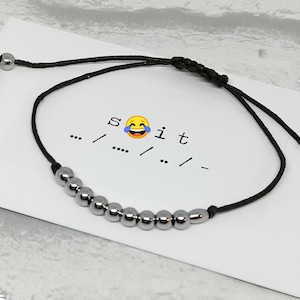 May include: A black string bracelet with silver beads and the text "s 😂 it ... / ... / ... / -" on a white card.