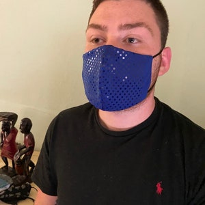 May include: A blue sequined face mask. The mask is made of a shiny, reflective material and covers the nose and mouth. The mask is worn by a person wearing a black shirt.