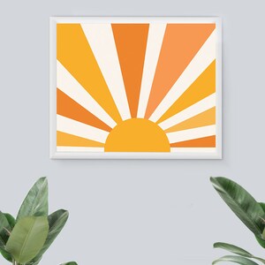 May include: A framed print of a stylized sun with orange, yellow, and white rays. The sun is a solid yellow color.
