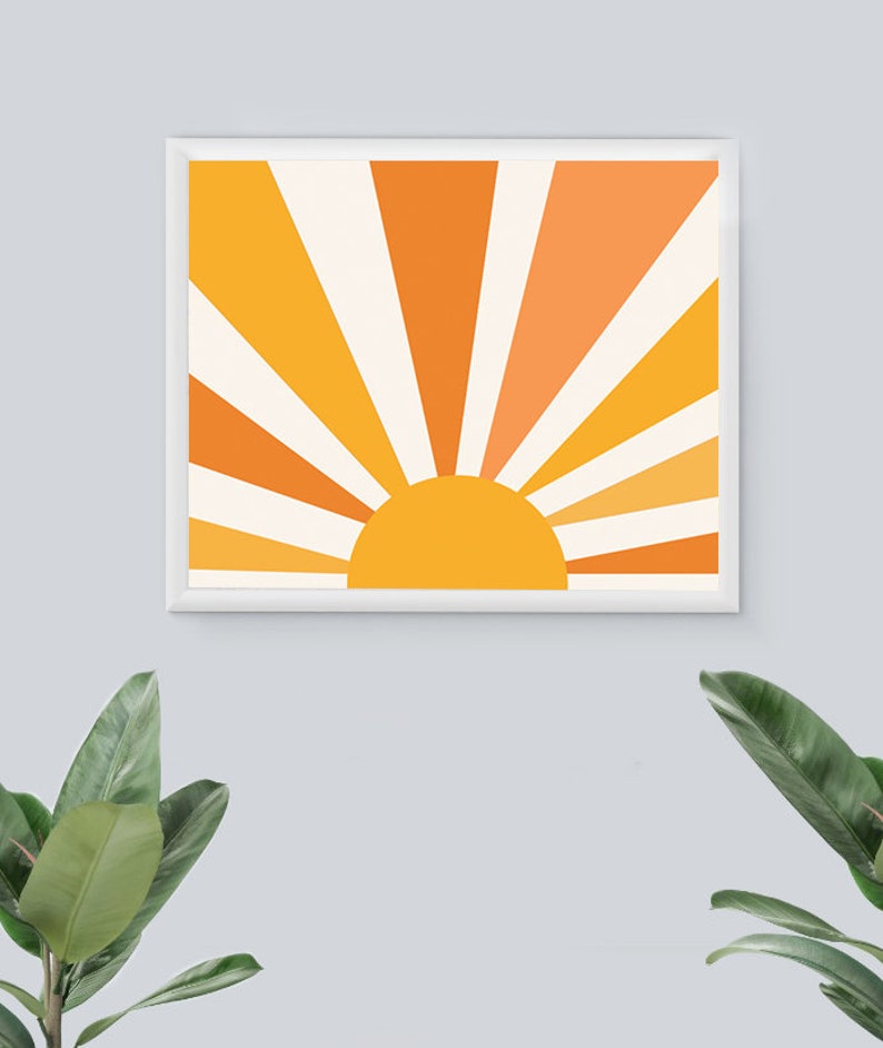 May include: A framed print of a stylized sun with orange, yellow, and white rays. The sun is a solid yellow color.