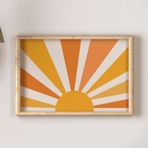 May include: A framed print of a stylized sun with orange, yellow, and white rays. The sun is set against a cream background.