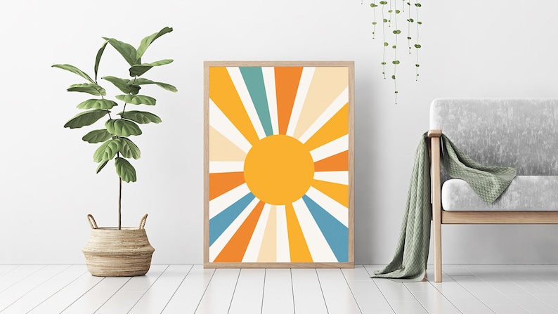 May include: A framed print of a stylized sun with orange, yellow, white, and blue rays. The sun is in the center of the print and is surrounded by rays that radiate outwards. The print is framed in a light wood frame.