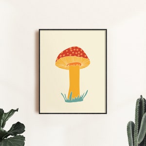 May include: A framed art print depicting a stylized mushroom illustration. The mushroom has a red cap with white spots, a yellow stem, and is set against a cream background. The artwork is framed in a black frame.