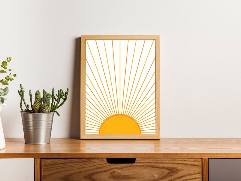 May include: A framed print of a stylized sun with yellow and orange rays on a white background. The frame is light wood.