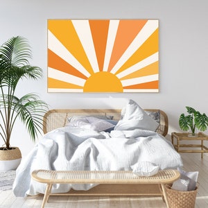 May include: A white bed with a wooden headboard and a white duvet. The bed is decorated with pillows and a throw blanket. A wooden bench sits at the foot of the bed. A large framed print of a stylized sun with orange and yellow rays hangs on the wall behind the bed.