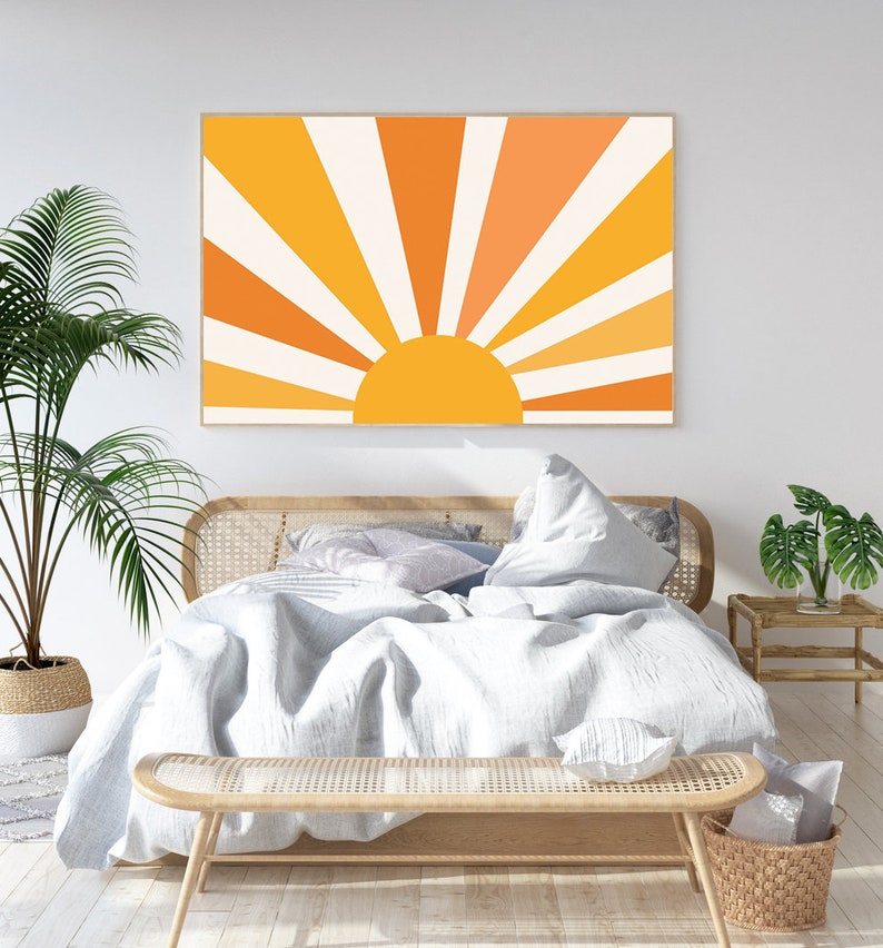 May include: A white bed with a wooden headboard and a white duvet. The bed is decorated with pillows and a throw blanket. A wooden bench sits at the foot of the bed. A large framed print of a stylized sun with orange and yellow rays hangs on the wall behind the bed.