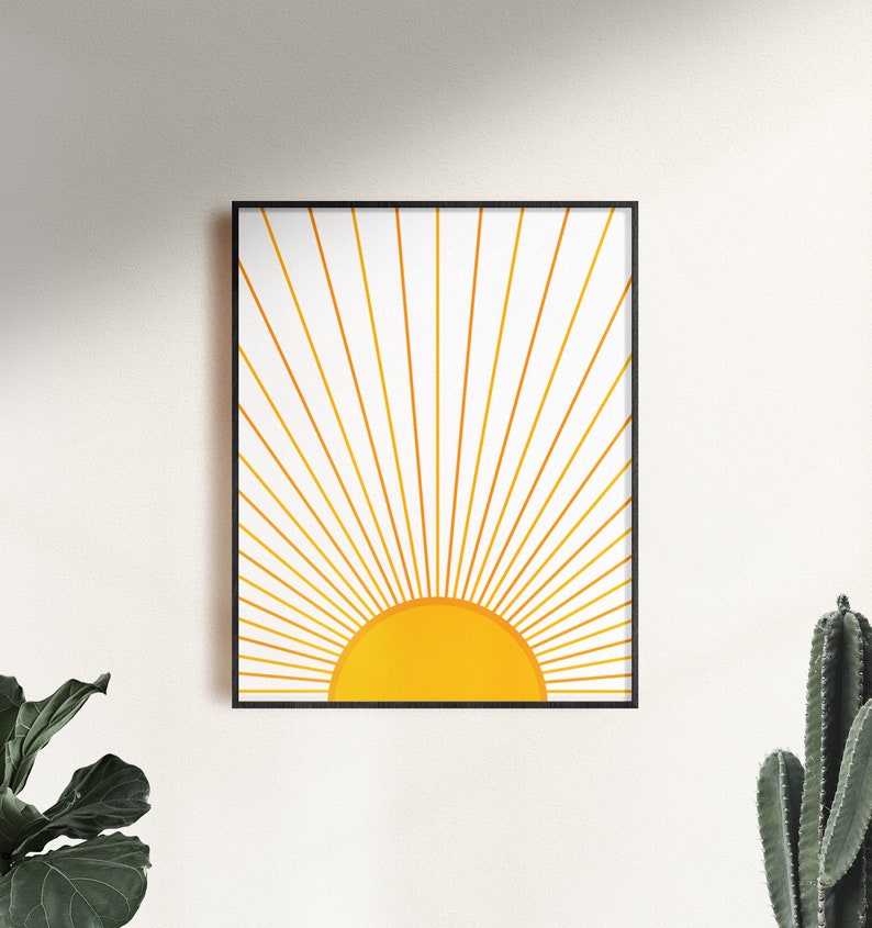 May include: A framed print of a minimalist sun design with gold rays and a yellow sun on a white background.