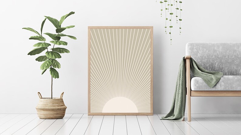 Puede incluir: Una impresi&oacute;n enmarcada de un dise&ntilde;o de sol beige con un sol blanco en el centro. La impresi&oacute;n est&aacute; colgada en una pared blanca con una planta verde en una cesta de mimbre y un sof&aacute; gris con una manta de tiro verde en primer plano.