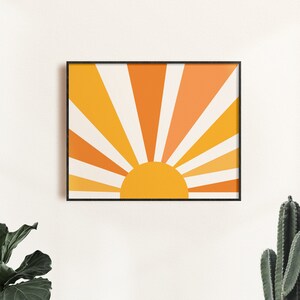 May include: A framed print of a stylized sun with orange and yellow rays radiating outward. The sun is a solid yellow circle.