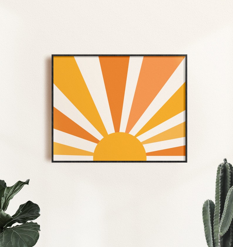 May include: A framed print of a stylized sun with orange and yellow rays radiating outward. The sun is a solid yellow circle.