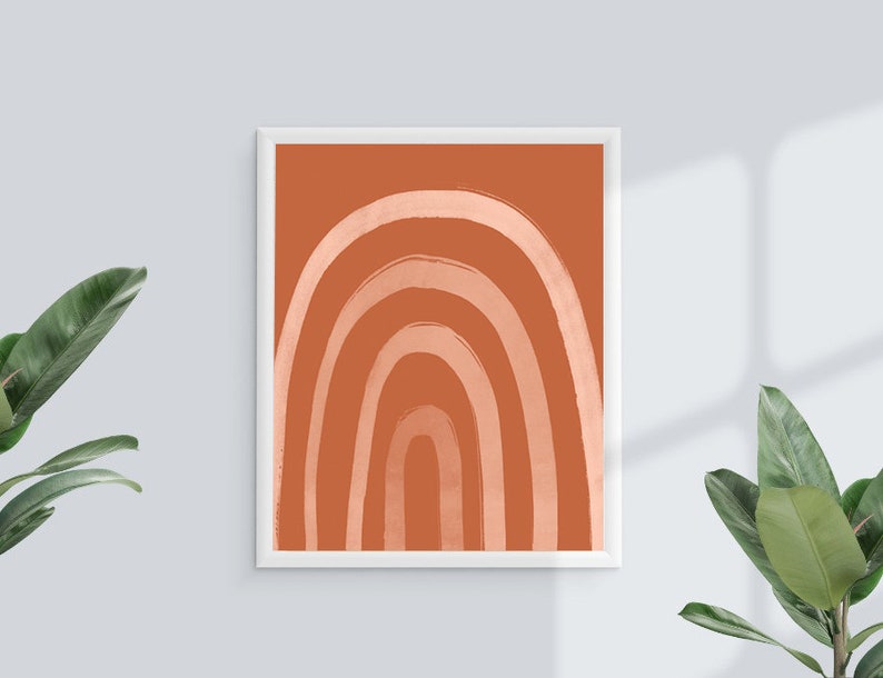 May include: A framed art print featuring a stylized rainbow design. The artwork showcases a series of curved lines in varying shades of orange and peach against a solid orange background. The print is encased in a white frame.