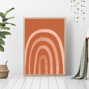 May include: A framed art print featuring an abstract rainbow design. The artwork showcases a series of curved lines in shades of peach and white against a terracotta background. The print is displayed in a light wood frame, suitable for home decor.