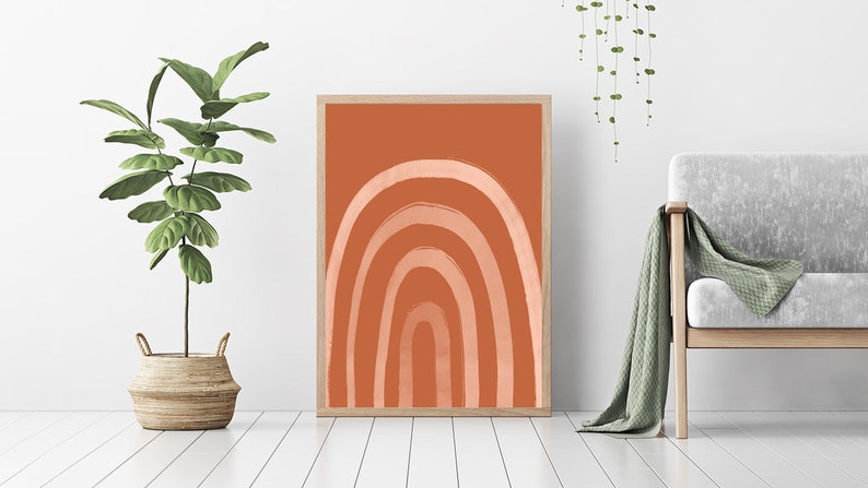 May include: A framed art print featuring an abstract rainbow design. The artwork showcases a series of curved lines in shades of peach and white against a terracotta background. The print is displayed in a light wood frame, suitable for home decor.