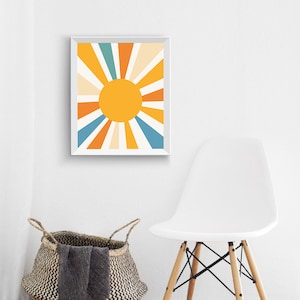 May include: A framed print of a stylized sun with orange, yellow, blue, and cream rays radiating outward from a yellow circle.