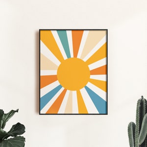 May include: A framed print of a stylized sun with orange, yellow, blue, and white rays. The sun is a solid yellow circle in the center of the print.