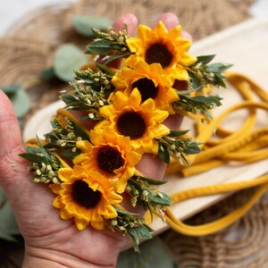 Op de afbeelding: Een mosterdgele zonnebloem haarband met vier felgele zonnebloemen en groene bladeren. De haarband is gemaakt van een zachte, mosterdkleurige stof. De bloemen hebben donkerbruine centra.