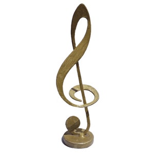 Puede incluir: Una escultura de clave de sol de metal dorado con una base redonda. La escultura es una pieza decorativa para el hogar de un amante de la música.