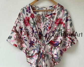 May include: A white cotton dress with a floral print featuring red, pink, blue, and green flowers and birds. The dress has a V-neckline and short sleeves. The dress is tied at the waist with a knot.